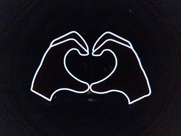 A warm illustration of two hands reaching out with a pink heart glowing between them on a clean white background.