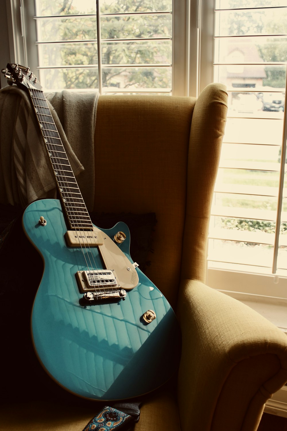 a blue guitar sitting on top of a chair next to a window