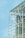 A modern architectural structure features a glass facade with visible steel beams and supports, offering a transparent view of the building's interior framework against a clear blue sky. The design emphasizes sleek lines and industrial elements.