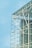 A modern architectural structure features a glass facade with visible steel beams and supports, offering a transparent view of the building's interior framework against a clear blue sky. The design emphasizes sleek lines and industrial elements.