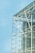 A modern architectural structure features a glass facade with visible steel beams and supports, offering a transparent view of the building's interior framework against a clear blue sky. The design emphasizes sleek lines and industrial elements.