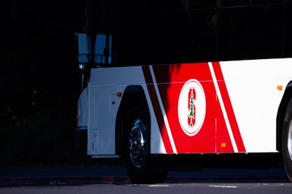 The side view of a bus featuring a distinctive logo with a red and white color scheme. The logo includes a green tree emblem, placed on a section of the bus with red diagonal stripes.