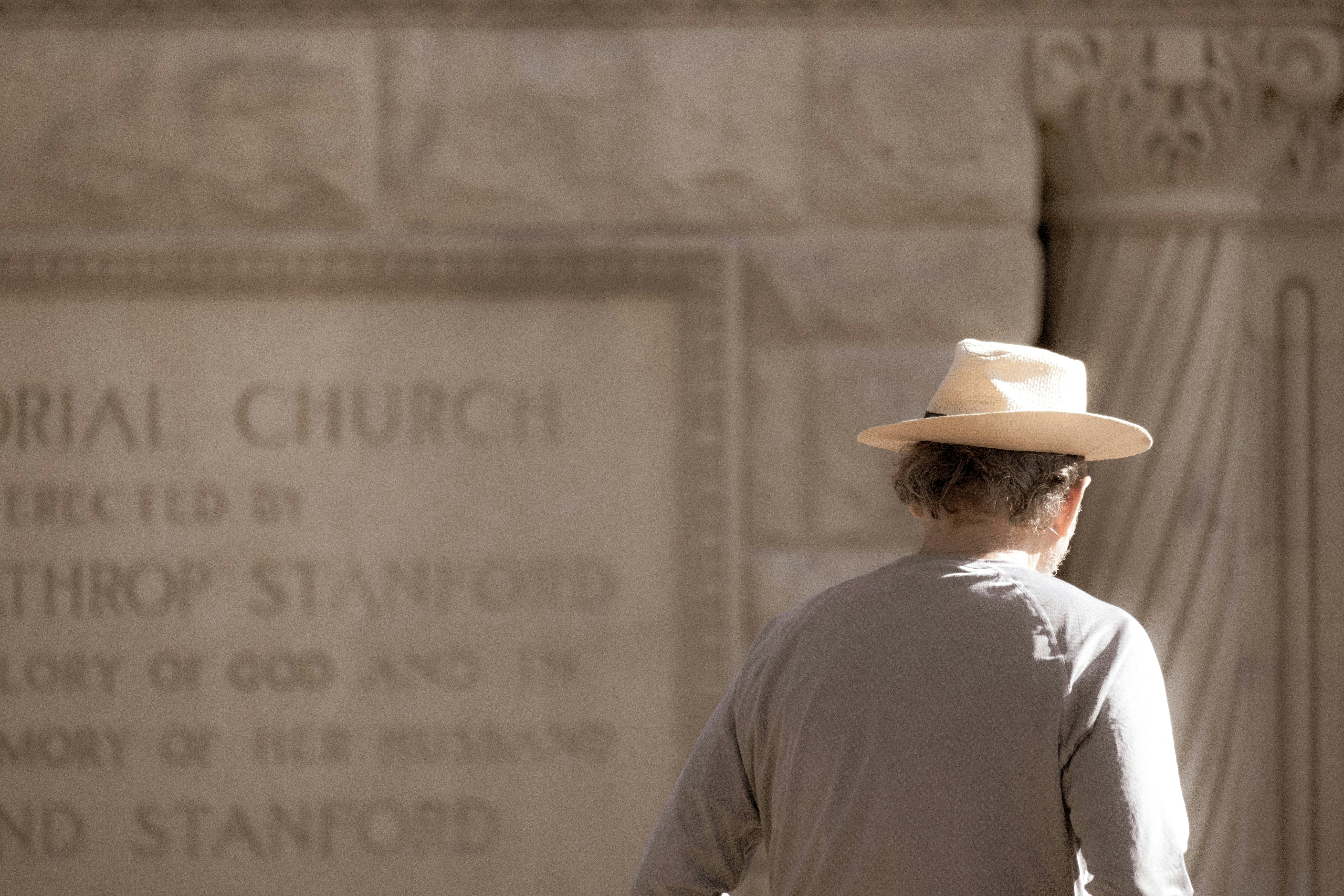 a man wearing a hat walking in front of a memorial