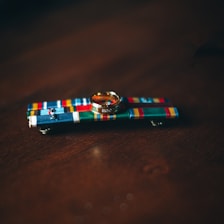 A gold ring rests on a colorful military ribbon bar with various patterns and stripes against a dark wooden surface.
