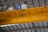 A drone is flying indoors near a large yellow overhead crane with a visible signage indicating 32t. The ceiling structure features metal beams and industrial lighting.