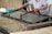 A person is engaged in traditional paper-making, using a wooden frame to scoop up a sheet of pulp from a water vat. The setting seems artisanal, with tools and materials neatly arranged around. The process appears to be taking place in a workshop-like environment.