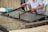A person is engaged in traditional paper-making, using a wooden frame to scoop up a sheet of pulp from a water vat. The setting seems artisanal, with tools and materials neatly arranged around. The process appears to be taking place in a workshop-like environment.