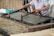 A person is engaged in traditional paper-making, using a wooden frame to scoop up a sheet of pulp from a water vat. The setting seems artisanal, with tools and materials neatly arranged around. The process appears to be taking place in a workshop-like environment.