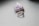A silver ring with an ornate design is placed on a smooth, light gray surface. Behind it is a piece of raw amethyst crystal, displaying a vibrant purple color with a rough texture.