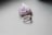 A silver ring with an ornate design is placed on a smooth, light gray surface. Behind it is a piece of raw amethyst crystal, displaying a vibrant purple color with a rough texture.