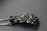 An intricately designed metallic hand sculpture featuring detailed wirework and spherical accents, with a central green stone. The craftsmanship highlights an organic but mechanical aesthetic with a matte finish.