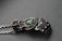 An intricately designed metallic hand sculpture featuring detailed wirework and spherical accents, with a central green stone. The craftsmanship highlights an organic but mechanical aesthetic with a matte finish.