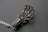 A metallic sculpture resembling a hand, composed of intricate wirework and small spherical elements, is placed on a textured dark surface. The fingers are elongated and structured in a mechanical, futuristic design.