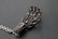 A metallic sculpture resembling a hand, composed of intricate wirework and small spherical elements, is placed on a textured dark surface. The fingers are elongated and structured in a mechanical, futuristic design.