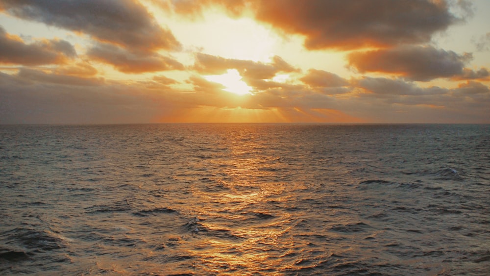 the sun is setting over the ocean on a cloudy day