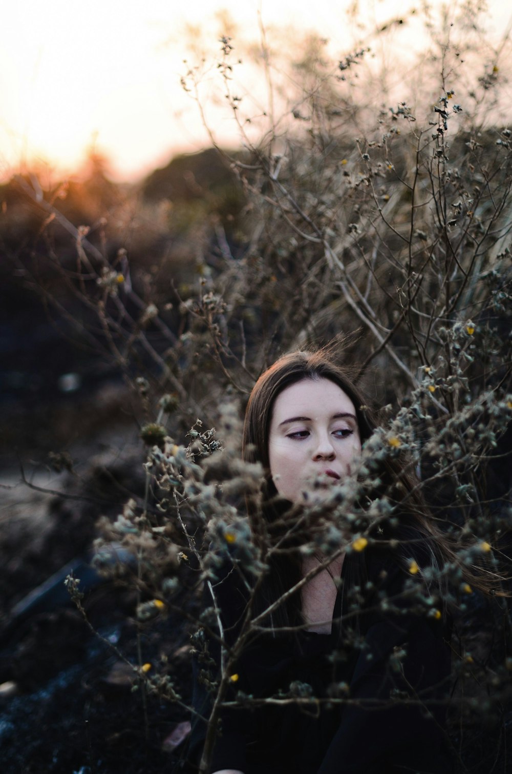 Una mujer está sentada en un arbusto con los ojos cerrados