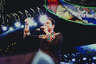 Artist performing live with expressive gestures under colorful stage lights.