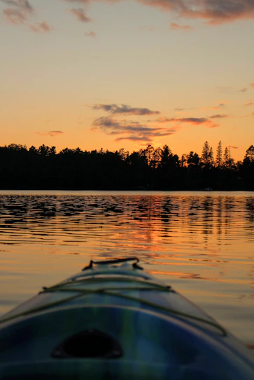 Sunlight sparkling on calm coastal waters as a kayak glides past marsh grasses at golden hour.