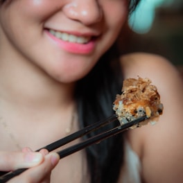 A smiling server handing over a takeout box of sushi with chopsticks.