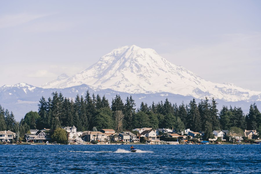 Mount Rainier rising over a fir-lined row of waterfront homes across open water