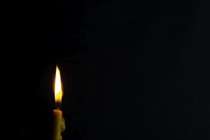 Close-up of a minimalist handmade candle with a soft glowing flame on a wooden table.