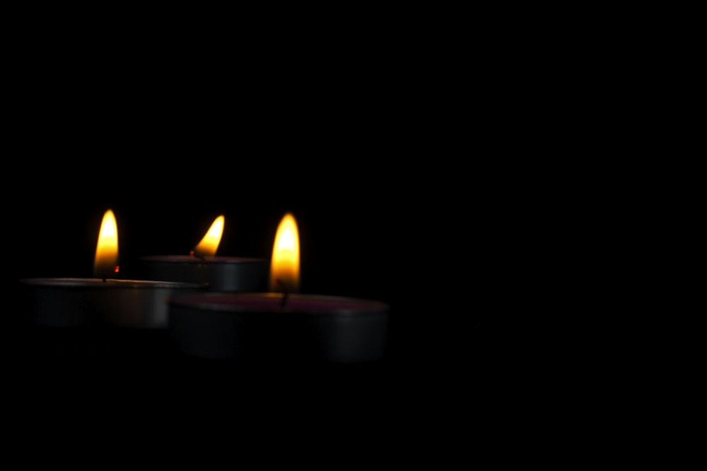 three lit candles in a dark room
