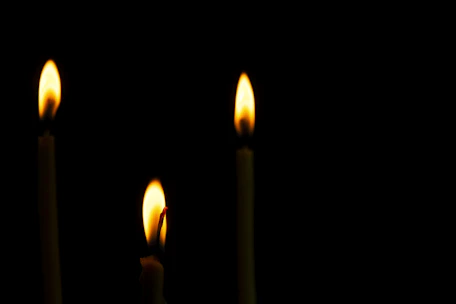Close-up of three star-shaped candle flames flickering gently in a dark room.