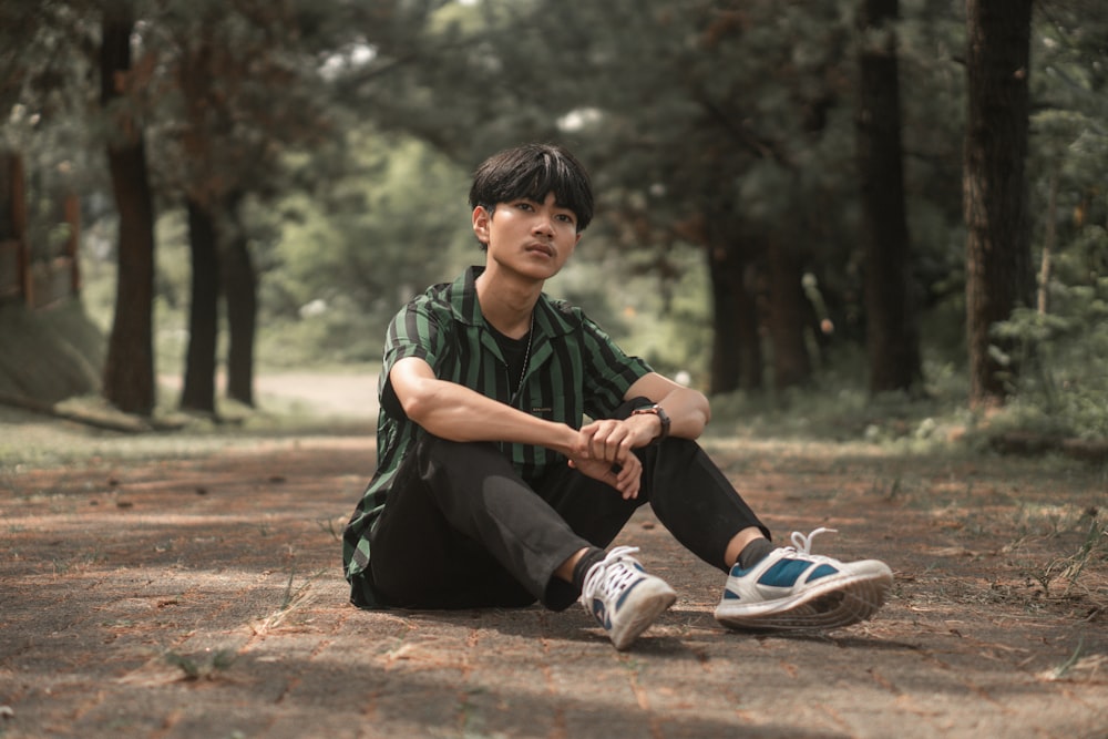 a young man sitting on the ground in the woods