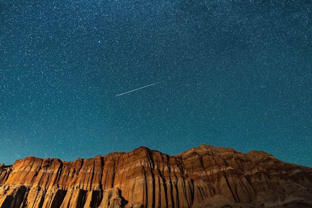 Un cielo nocturno con un avión volando sobre una montaña