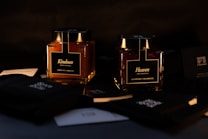 Two elegantly designed jars labeled 'Kindness' and 'Heaven,' containing apricot and raspberry products respectively, are placed against a dark background. The lighting highlights the rich colors of the contents, providing a luxurious and sophisticated atmosphere. Around the jars are various black and white cards with intricate designs.