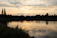 A serene lakeside at sunset with gentle ripples reflecting soft orange and pink hues.