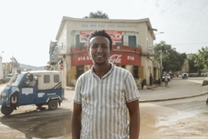 A smiling rickshaw driver proudly standing beside his new electric rickshaw in a busy Uttar Pradesh street.