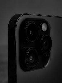 A close-up view of a smartphone's camera module, featuring multiple lenses and a flash. The image is dominated by dark shades, emphasizing the glossy surface of the phone.