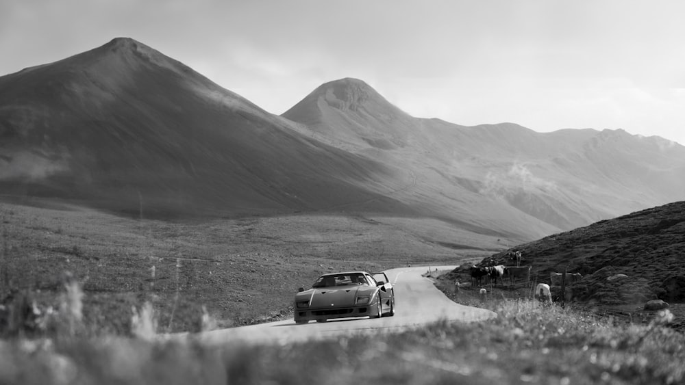 a black and white photo of a car driving down a mountain road