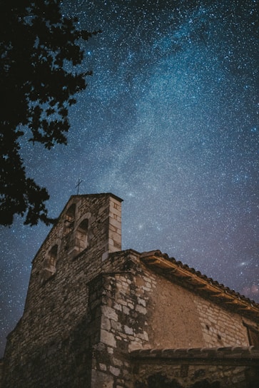A serene night sky with stars shining over a minimalist blue and gold church building.