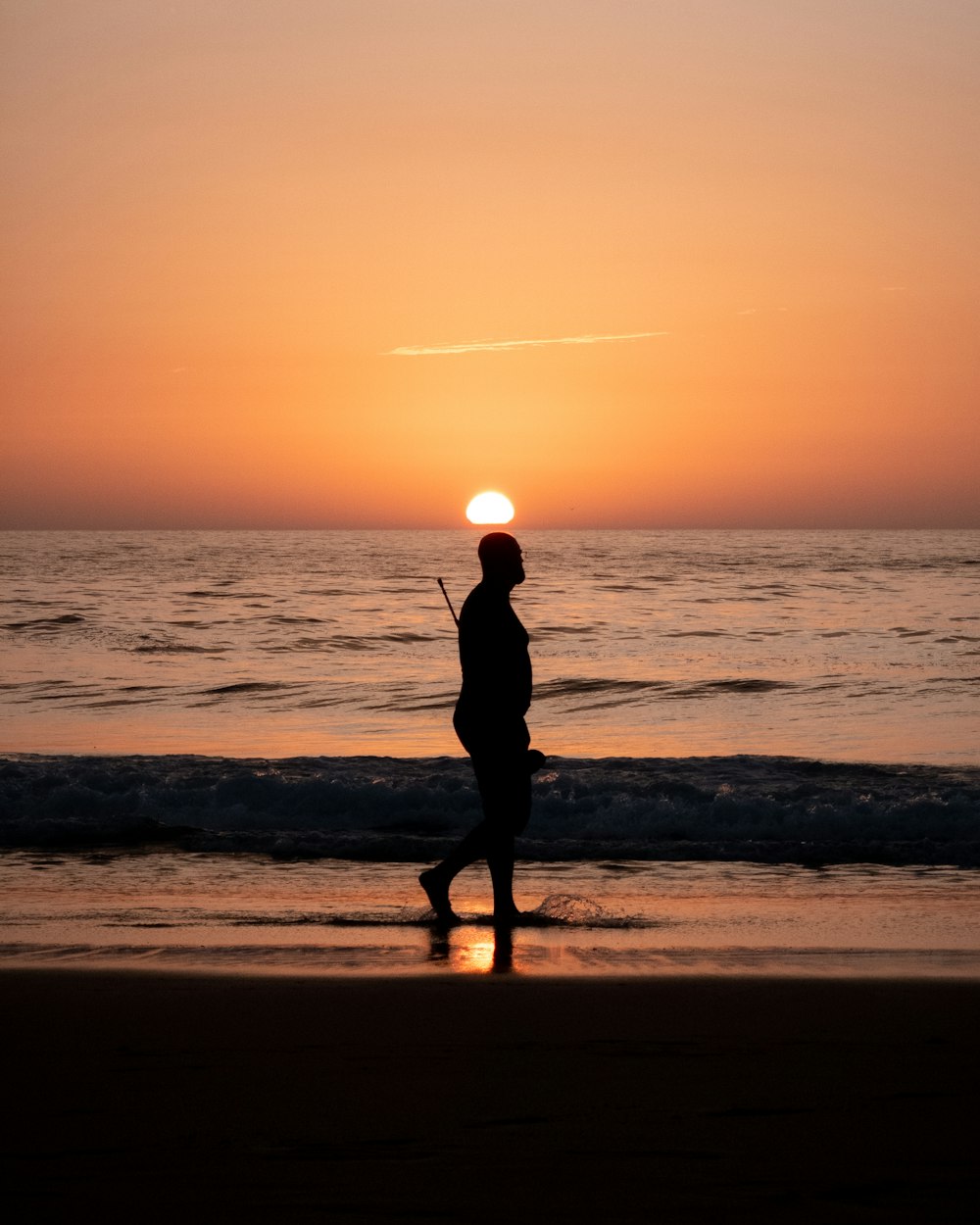 une personne marchant sur la plage au coucher du soleil