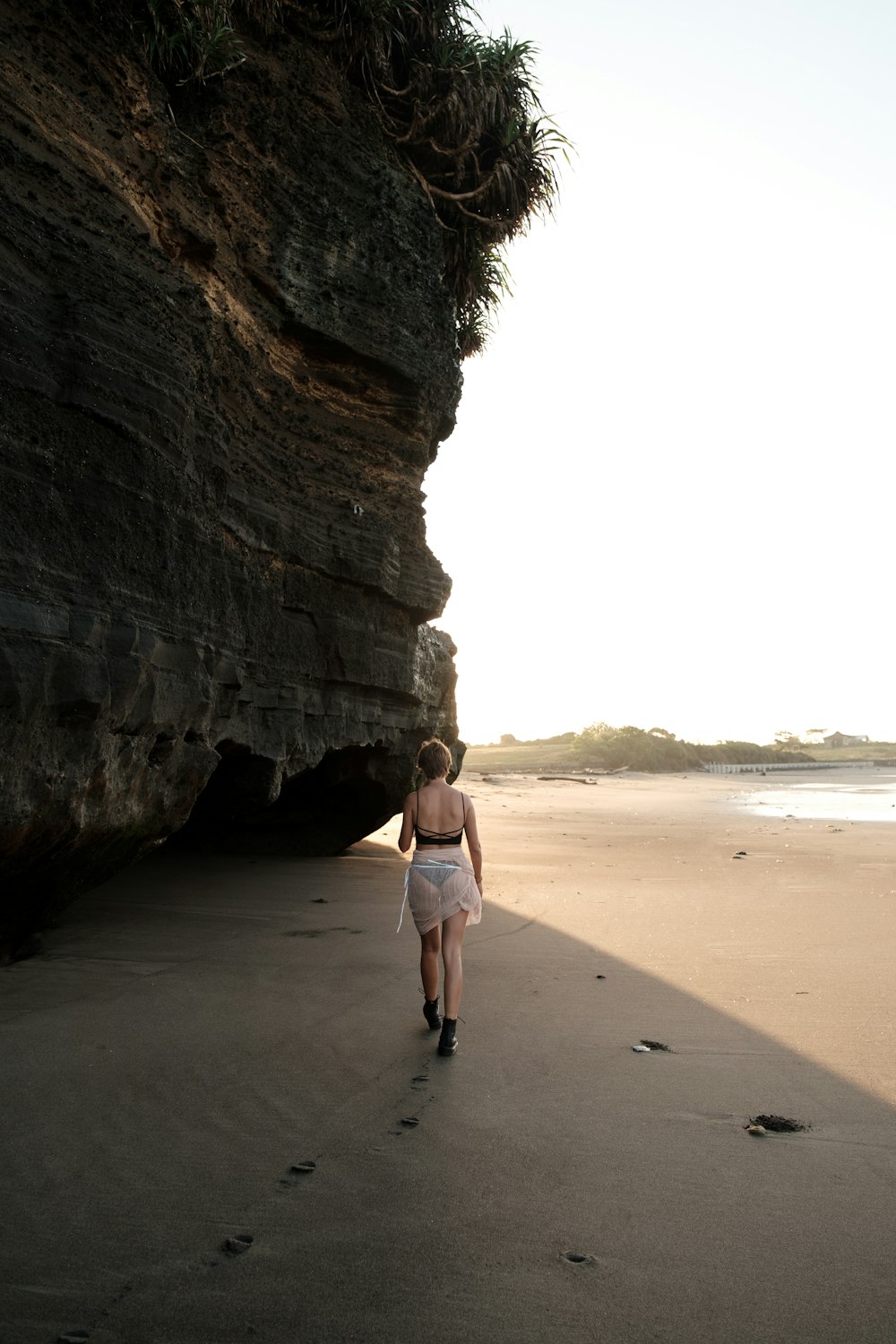 a woman walking on a beach next to a cliff