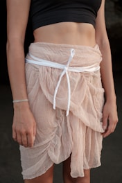 A person wearing a black cropped top and a light pink sheer skirt tied with a white ribbon. The fabric has a soft, flowing texture, and the skirt is layered, providing an elegant appearance.