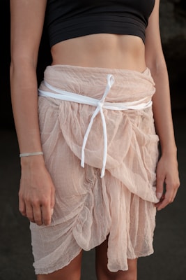 A person wearing a black cropped top and a light pink sheer skirt tied with a white ribbon. The fabric has a soft, flowing texture, and the skirt is layered, providing an elegant appearance.