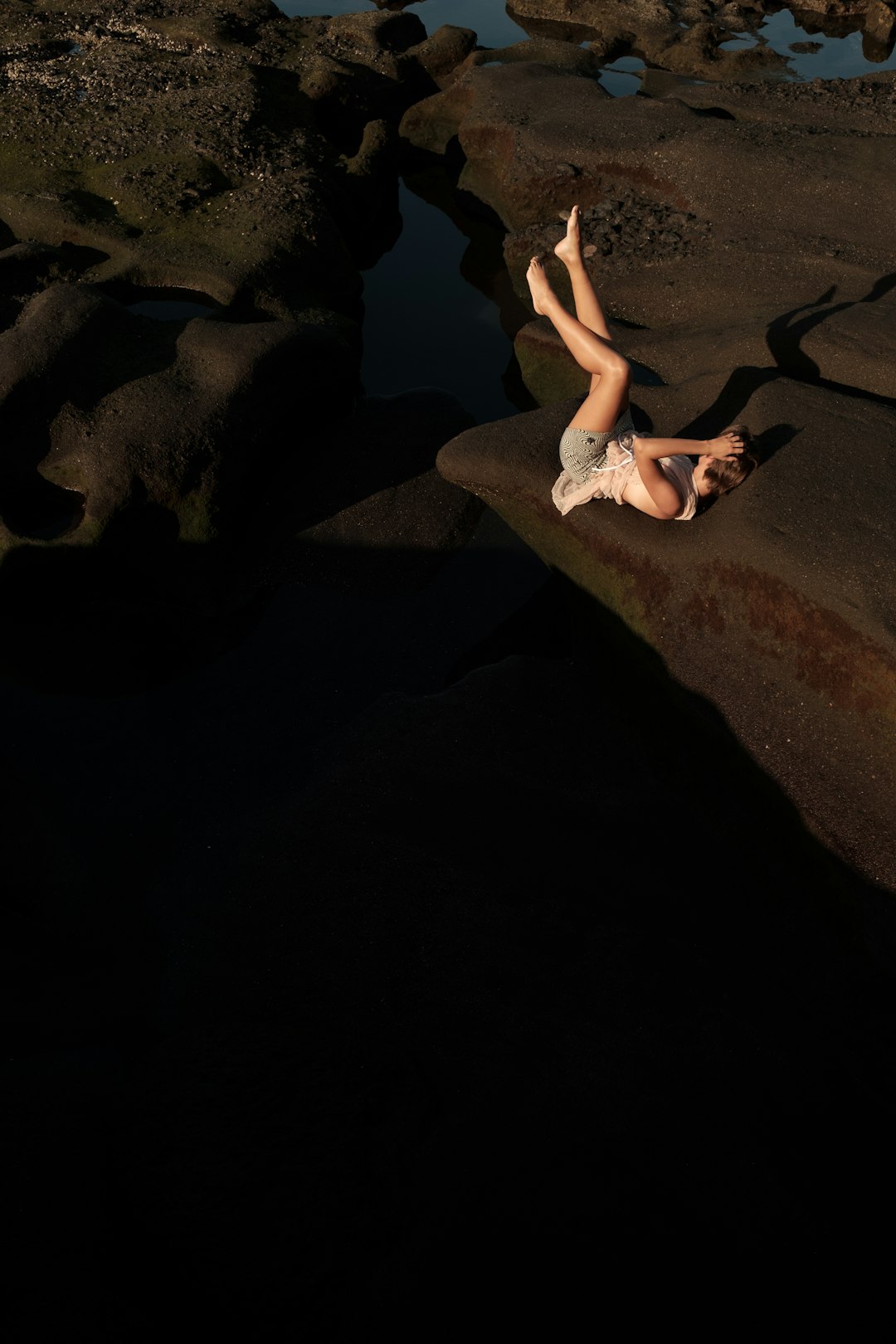 a woman laying on a rock next to a body of water