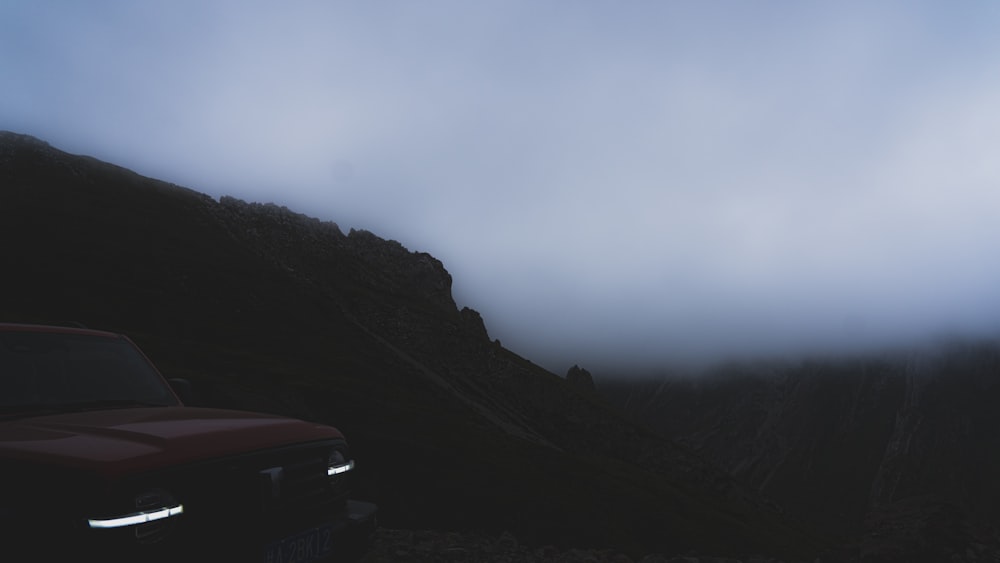 a red car driving down a road next to a mountain