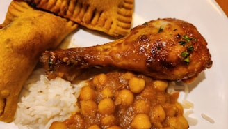 A plate of food featuring a cooked drumstick, chickpea curry, white rice, and a fried pastry.