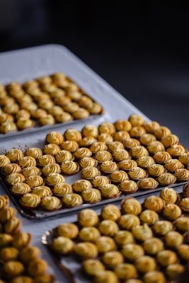 Rows of intricately swirled, baked pastries arranged on trays resting on a table covered with a white cloth. The pastries are small, golden brown, and uniform in shape.