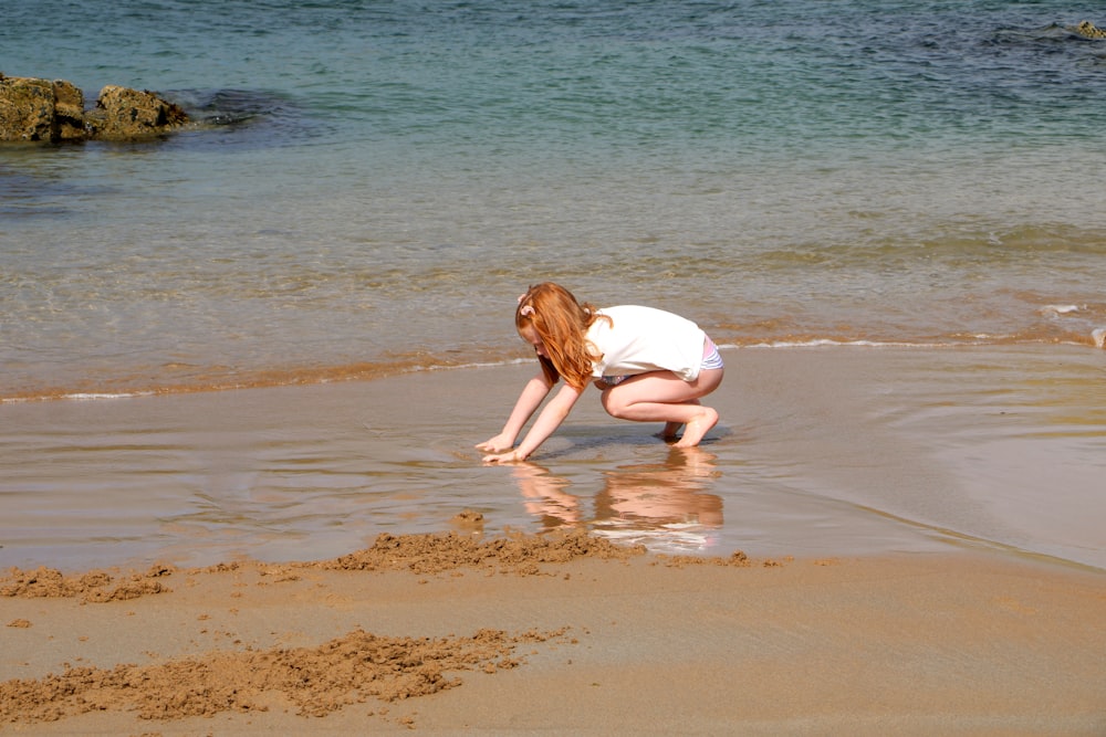 a woman kneeling down on top of a sandy beach