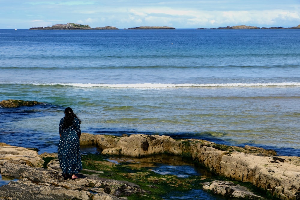 a woman standing on a rocky shore next to the ocean
