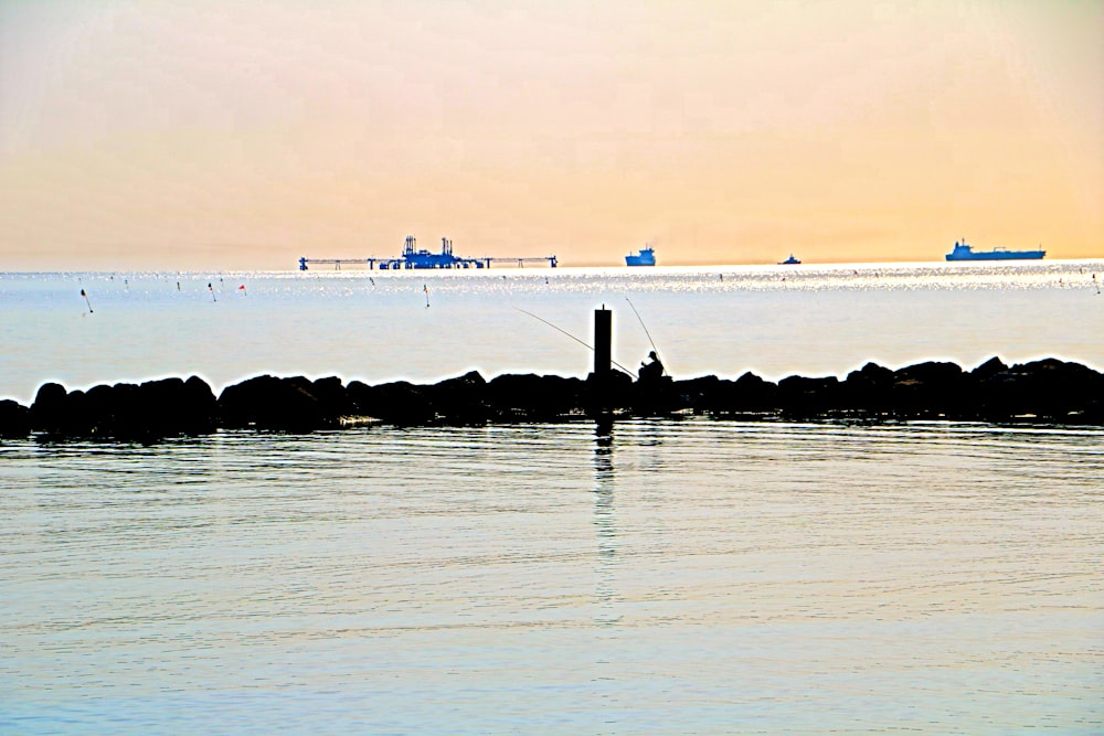 a man fishing on the water with a boat in the background