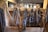 Various horse bridles and leather straps hang neatly in a wooden tack room. The wooden walls and beams give the space a rustic, historical feel.