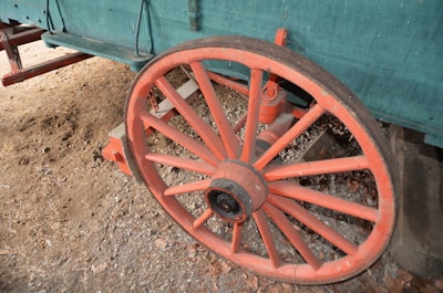 An old wooden wheel with eight spokes resting on a dirt road leading toward a distant mountain.