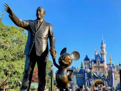 a statue of walt and mickey mouse in front of a castle
