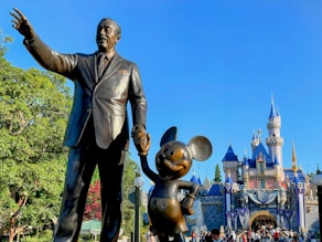 a statue of walt and mickey mouse in front of a castle